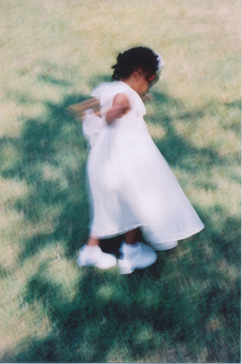 Soft, motion-blurred photograph of a child in a white dress moving through a grassy field.