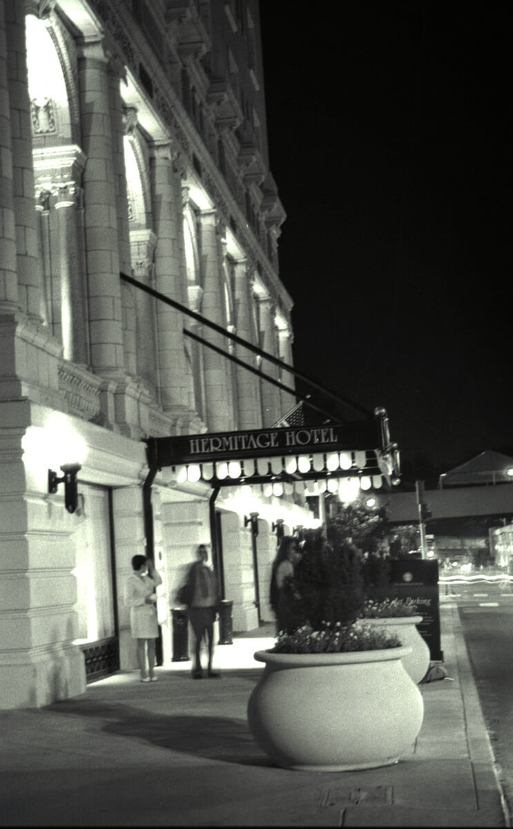 Black and white night photograph of the Hermitage Hotel entrance with glowing marquee and architectural columns.